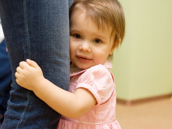 Shy baby girl hugging parents leg